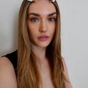 May include: A woman with long, light brown hair is wearing a black tank top. She has two small, white hair clips in her hair.