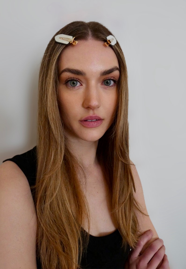 May include: A woman with long, light brown hair is wearing a black tank top. She has two small, white hair clips in her hair.