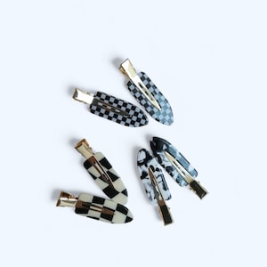 May include: Five hair clips in a variety of black and white patterns. The clips are made of plastic and have a gold metal clasp.