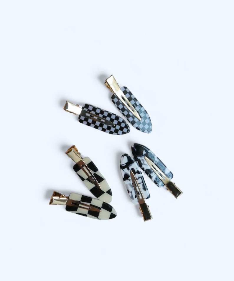 May include: Five hair clips in a variety of black and white patterns. The clips are made of plastic and have a gold metal clasp.