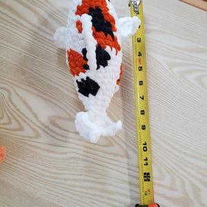 May include: A handmade crochet koi fish toy, featuring white, orange, and black patterns. The fish measures approximately 12 inches in length. The soft, plush design is ideal for children or as a decorative item.