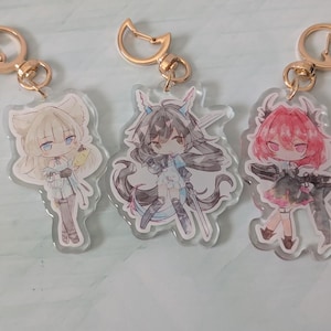 Pode incluir: Tr&ecirc;s chaveiros de acr&iacute;lico em estilo anime com fechos dourados. Cada chaveiro apresenta uma ilustra&ccedil;&atilde;o de personagem diferente em tons de branco, preto, rosa e azul. Os chaveiros s&atilde;o cortados em forma dos personagens.