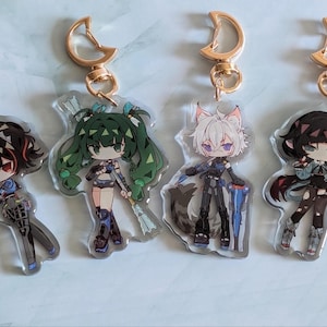Op de afbeelding: Vier anime-personage sleutelhangers met gouden metalen ringen. Elke sleutelhanger heeft een ander personage met unieke haar- en kledingstijlen. De personages zijn afgebeeld in een kleurrijke, cartoonachtige stijl.