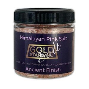 May include: A glass jar filled with pink Himalayan salt. The label reads "Himalayan Pink Salt", "Gold Standard Salt", "This salt does not supply iodide, a necessary nutrient", and "Ancient Finish".
