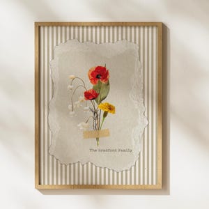 May include: A framed floral print featuring a bouquet of red poppies, yellow flowers, and white blossoms. The flowers are taped to a textured paper with the text "The Bradford Family". The frame has a striped background.