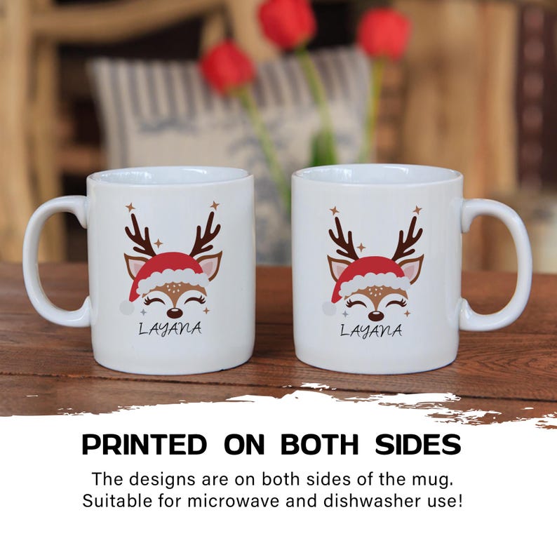 May include: Two white ceramic mugs with a reindeer design. The reindeer is wearing a red Santa hat and has a brown nose. The mugs have the name "Layana" printed on them. The mugs are printed on both sides.