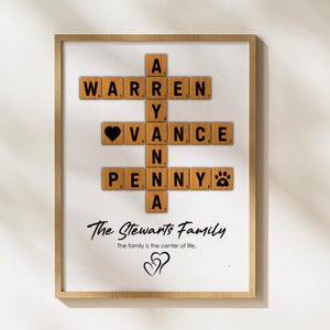 May include: A framed print with a wooden background featuring a scrabble tile crossword puzzle with the names Warren, Avery, Vance, and Penny. The text "The Stewarts Family" and "The family is the center of life." is below the puzzle.