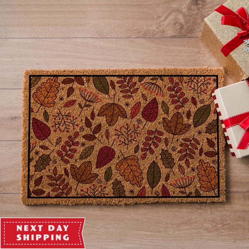 May include: A brown coir doormat with a black border featuring a pattern of colourful autumn leaves and branches.