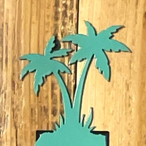 May include: Teal blue metal palm tree light switch cover. The cover is shaped like a palm tree with two palm fronds. The switch is in the center of the cover.