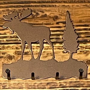 May include: Metal moose and pine tree silhouette wall hook with three hooks. The hook is brown and has a rustic look.