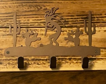 May include: A metal key rack with three hooks, featuring a silhouette of a Native American dancer surrounded by cacti. The rack is brown and has a rustic look.