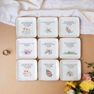 Puede incluir: Nueve platos cuadrados de cer&aacute;mica blanca con borde dorado y dise&ntilde;os florales. Cada plato tiene un mensaje personalizado para una madre, como "Estoy tan agradecida de tener una madre tan maravillosa. Te amo Mam&aacute;. Con amor, Ammy."
