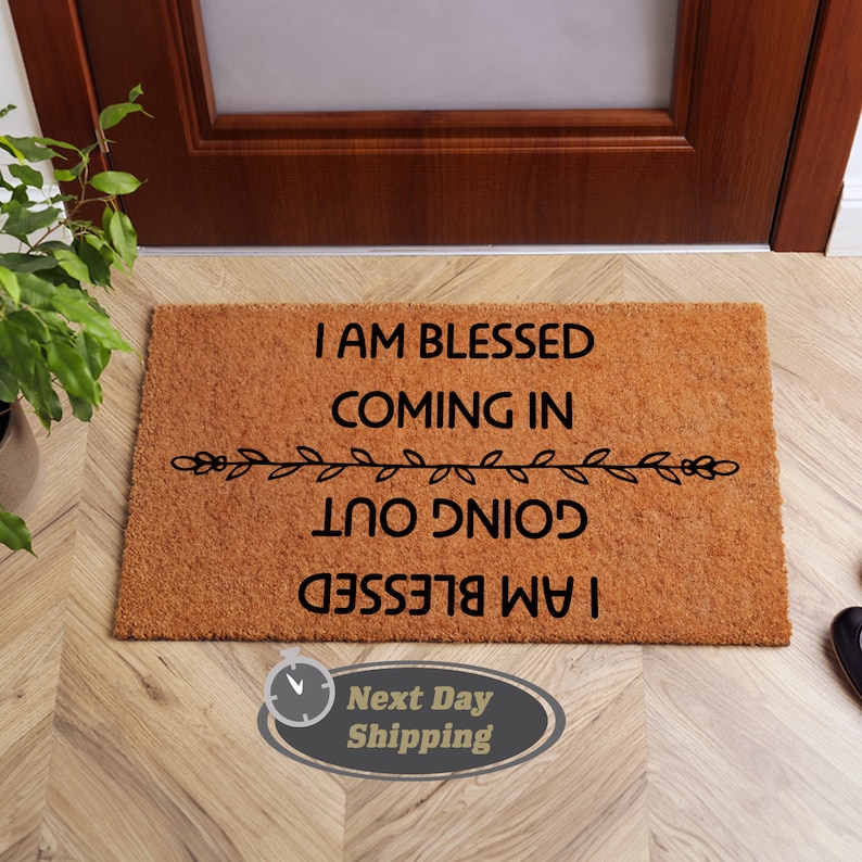May include: A brown coir doormat with the text "I am blessed coming in I am blessed going out" in black lettering. The text is framed by a decorative vine design.