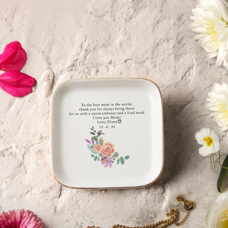 Puede incluir: Plato de cer&aacute;mica blanca para joyas con borde dorado. El plato presenta un dise&ntilde;o floral con flores rosas, moradas y verdes. El plato tiene un mensaje que dice "To the best mom in the world, thank you for always being there for us with a warm embrace and a kind word I love you Mom! Love, Diana 13.6.24"