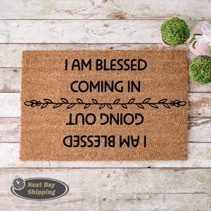 May include: A brown coir doormat with the text "I am blessed coming in going out I am blessed" in black lettering. The text is framed by a simple black vine design.