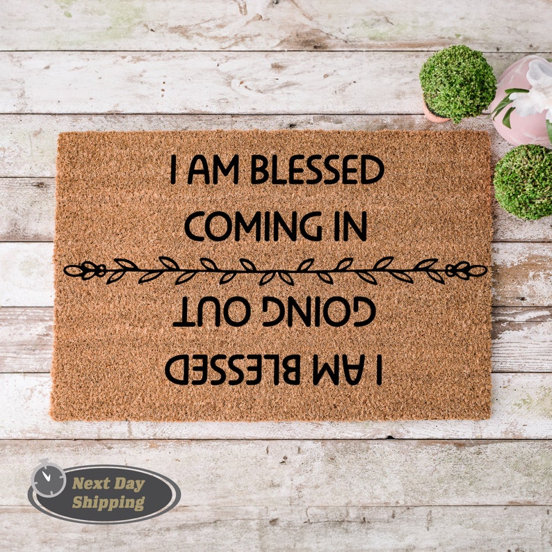May include: A brown coir doormat with the text "I am blessed coming in going out I am blessed" in black lettering. The text is framed by a simple black vine design.