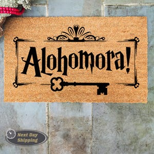 May include: A brown coir doormat with the text "Alohomora!" in black lettering with a decorative key design.