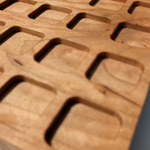 Peut inclure: Gros plan sur un plateau en bois avec un motif quadrillé d'espaces rectangulaires en retrait. Le plateau est en bois de couleur claire avec une finition lisse. Le design présente un motif répétitif de découpes rectangulaires.