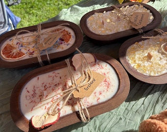 May include: Four oval wooden dough bowls filled with white wax candles. Each candle features unique toppings like dried orange slices, apple slices, or yellow crystals. Each bowl is tied with twine and a small brown paper tag with handwritten text.