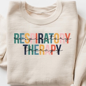 May include: A beige sweatshirt with the text "RESPIRATORY THERAPY" printed in colorful letters. The letters are in different colors, including pink, orange, yellow, green, and blue.