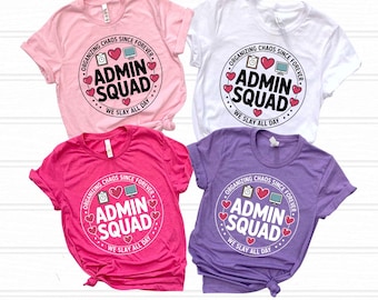 May include: Four short-sleeve t-shirts in light pink, white, hot pink, and lavender. Each shirt features a circular graphic with the text "ADMIN SQUAD", "ORGANIZING CHAOS SINCE FOREVER", and "WE SLAY ALL DAY", accompanied by icons of a clipboard, heart, and computer.