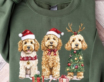 May include: A green sweatshirt with a Christmas-themed design featuring three dogs wearing festive attire. The dogs are wearing Santa hats, reindeer antlers, and a Christmas tree costume. The sweatshirt has a crew neck and long sleeves.