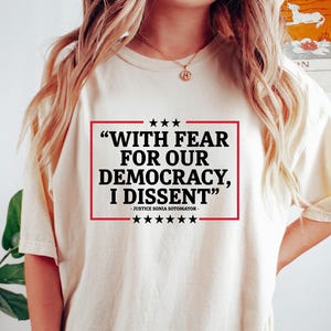 Può includere: Una maglietta bianca con una stampa grafica nera e rossa che recita "WITH FEAR FOR OUR DEMOCRACY, I DISSENT" - JUSTICE SONIA SOTOMAYOR.