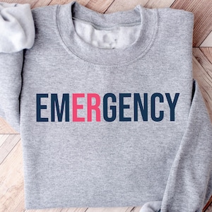 May include: Gray sweatshirt with the word "EMERGENCY" printed in navy blue and red letters.