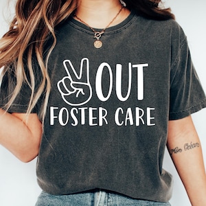 Op de afbeelding: Een grijs T-shirt met een wit peace-teken en de tekst "You Out Foster Care".
