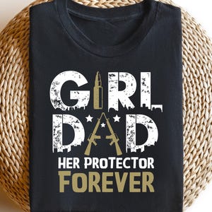 May include: Black t-shirt with white text that reads "Girl Dad Her Protector Forever". The text is surrounded by a gold bullet and two gold guns.