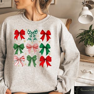 May include: A grey sweatshirt with a festive design featuring nine red, green and white bows with gold stars. The bows are arranged in a grid pattern on the front of the sweatshirt.