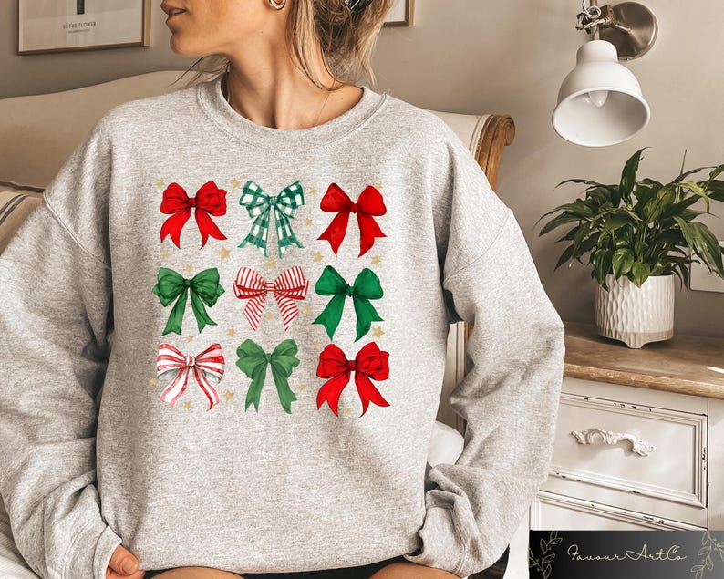 May include: A grey sweatshirt with a festive design featuring nine red, green and white bows with gold stars. The bows are arranged in a grid pattern on the front of the sweatshirt.