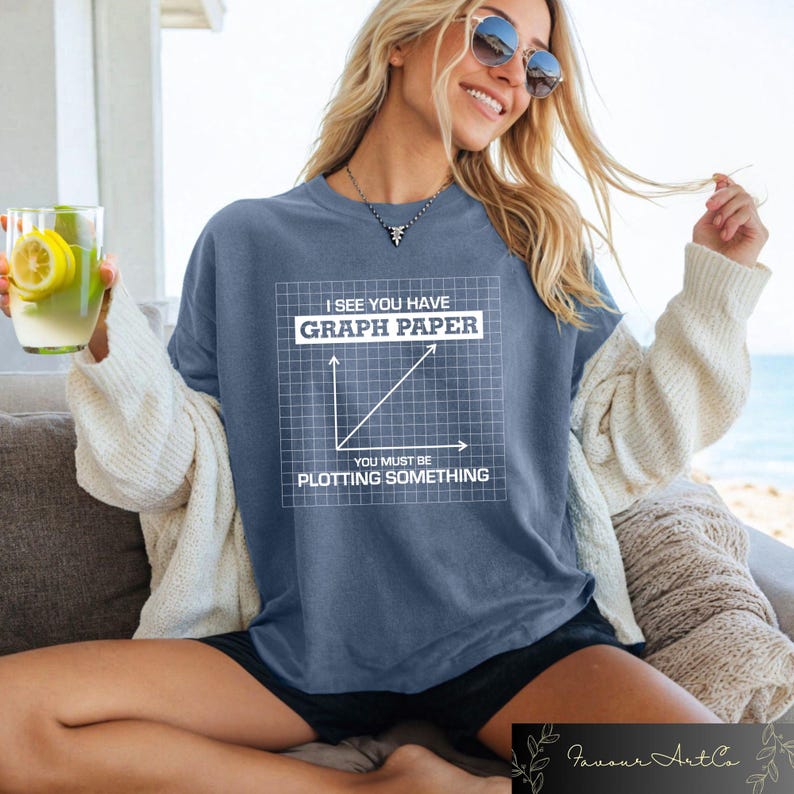 May include: A blue t-shirt with the text "I SEE YOU HAVE GRAPH PAPER, YOU MUST BE PLOTTING SOMETHING" and a graph design. The shirt is a relaxed fit and has short sleeves. The shirt is a solid blue color.