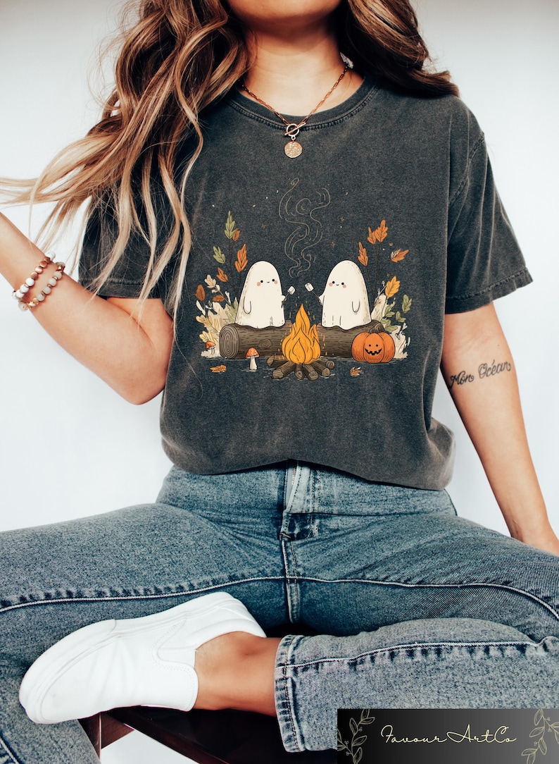 Puede incluir: Camiseta gris oscuro con una ilustraci&oacute;n de dos fantasmas blancos asando malvaviscos sobre una fogata. El dise&ntilde;o incluye un tronco, una calabaza y hojas de oto&ntilde;o, ideal para Halloween o el oto&ntilde;o.