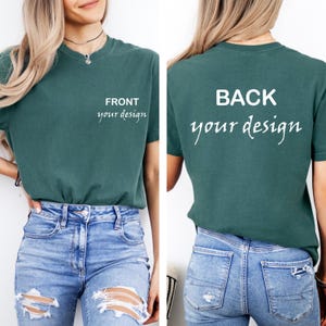 Puede incluir: Camiseta de color verde azulado con el texto "FRONT your design" en la parte delantera y "BACK your design" en la parte trasera. La camiseta es de color liso y tiene cuello redondo. El modelo lleva vaqueros azules.