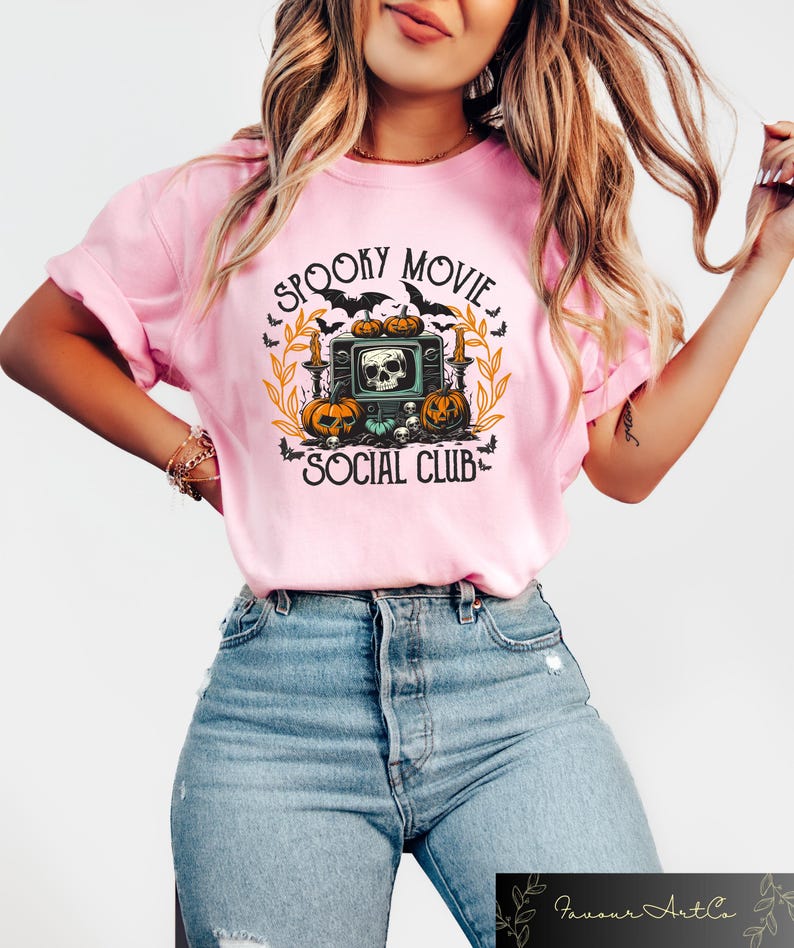 Puede incluir: Camiseta rosa claro con un dise&ntilde;o de Halloween. El dise&ntilde;o presenta una calavera dentro de un televisor retro, calabazas, murci&eacute;lagos y el texto "Spooky Movie Social Club."