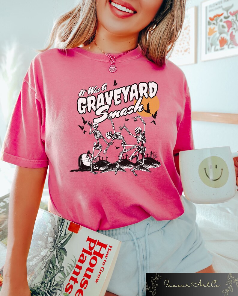 K&ouml;nnte beinhalten: Pinkes T-Shirt mit einem Grafikdruck von Skeletten, die auf einem Friedhof tanzen, mit dem Text "It Was A GRAVEYARD Smash".