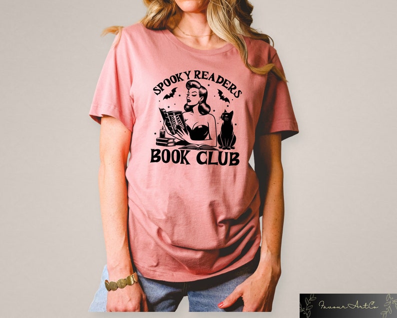 May include: A pink t-shirt with a black graphic of a woman reading a book with a black cat sitting next to her. The graphic says "Spooky Readers Book Club".