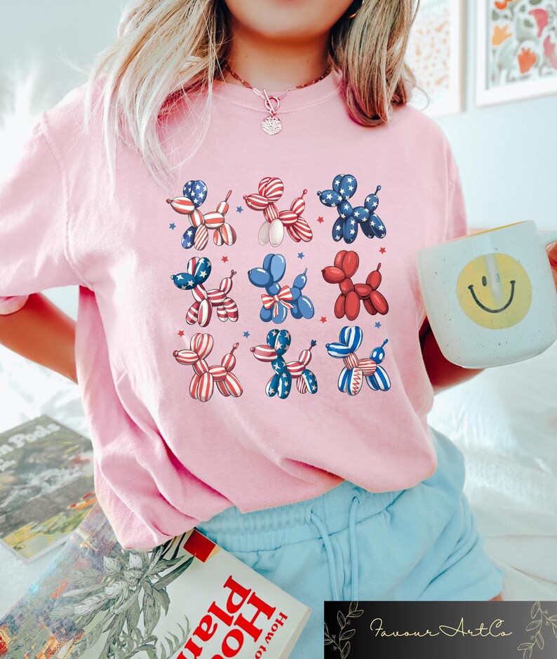K&ouml;nnte beinhalten: Ein hellrosa T-Shirt mit einem sich wiederholenden Muster aus Ballonhund-Designs in Rot, Wei&szlig; und Blau, mit Sternakzenten. Das Shirt ist ein l&auml;ssiger Stil, geeignet f&uuml;r den Alltag.