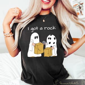 May include: Black t-shirt with a white graphic of two ghosts holding trick-or-treat bags. The text "I got a rock" is printed above the ghosts.