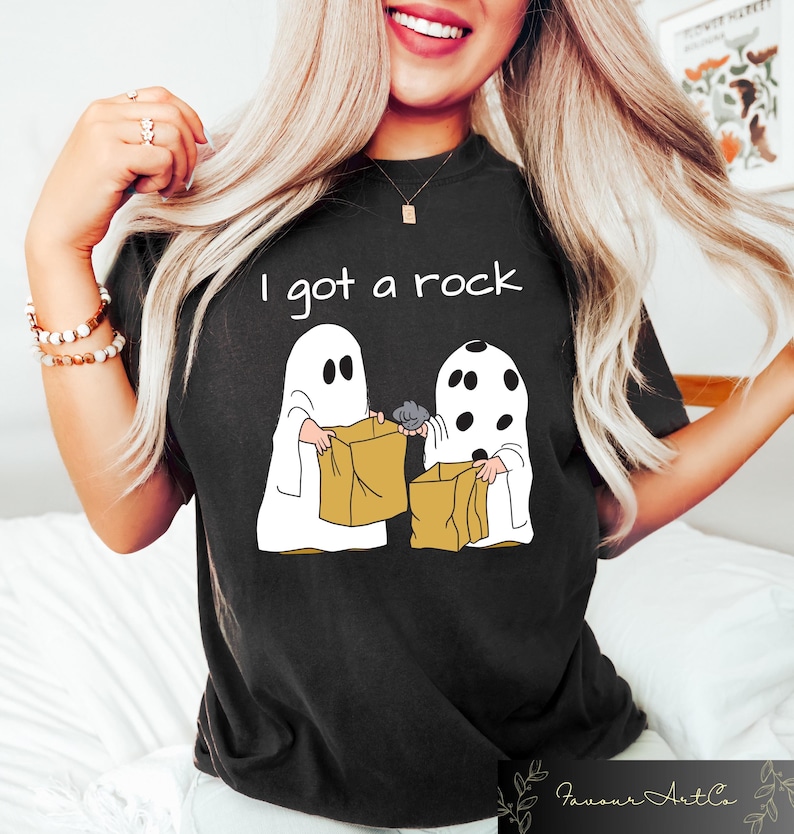May include: Black t-shirt with a white graphic of two ghosts holding trick-or-treat bags. The text "I got a rock" is printed above the ghosts.