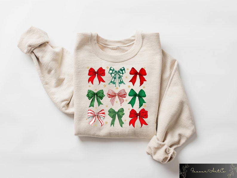 May include: A beige sweatshirt featuring a festive design of red and green bows with gold stars. The bows are arranged in a grid pattern.