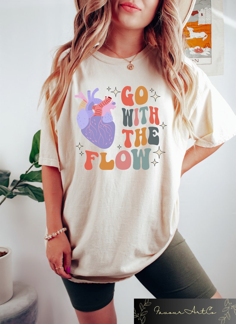 May include: A white t-shirt with a colorful graphic of a heart and the text "GO WITH THE FLOW" in a retro font.