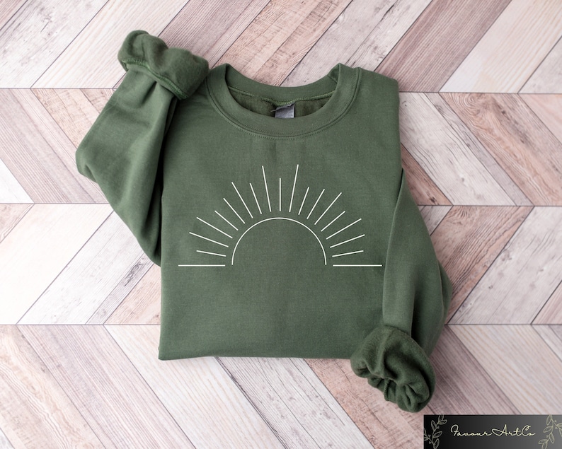 May include: A green sweatshirt with a white outline of a sun with rays.