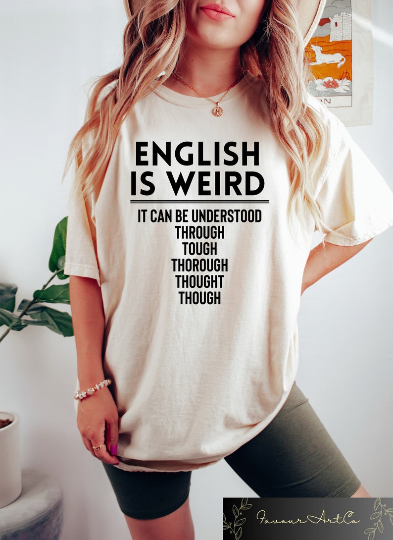 May include: A white t-shirt with the text "ENGLISH IS WEIRD" and the phrase "IT CAN BE UNDERSTOOD THROUGH TOUGH THOROUGH THOUGHT THOUGH" printed in black.