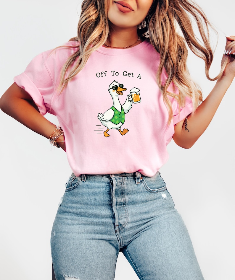 May include: Pink t-shirt with the text "Off To Get A" above a cartoon goose wearing sunglasses and a green vest, holding a beer. The goose is walking with motion lines.