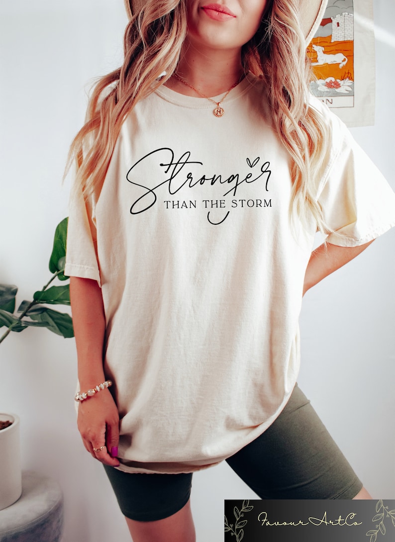 May include: A white t-shirt with the text "Stronger than the storm" in black cursive lettering with a small heart symbol.