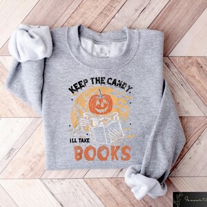 Op de afbeelding: Grijs sweatshirt met een pompoenprint en de tekst "Keep the candy, I'll take books".