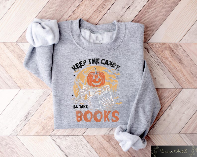 Op de afbeelding: Grijs sweatshirt met een pompoenprint en de tekst "Keep the candy, I'll take books".