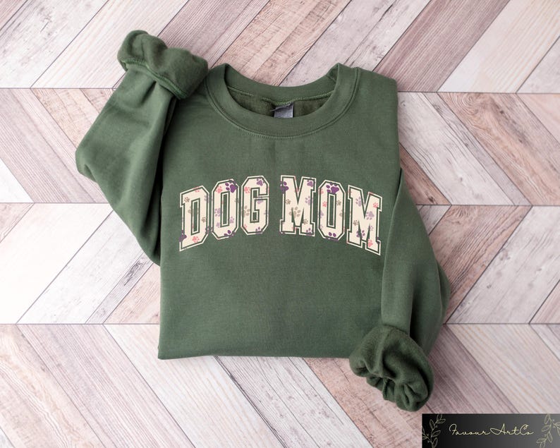 May include: A green sweatshirt with the text "DOG MOM" in a floral print. The text is in a large, bold font and is centered on the sweatshirt.